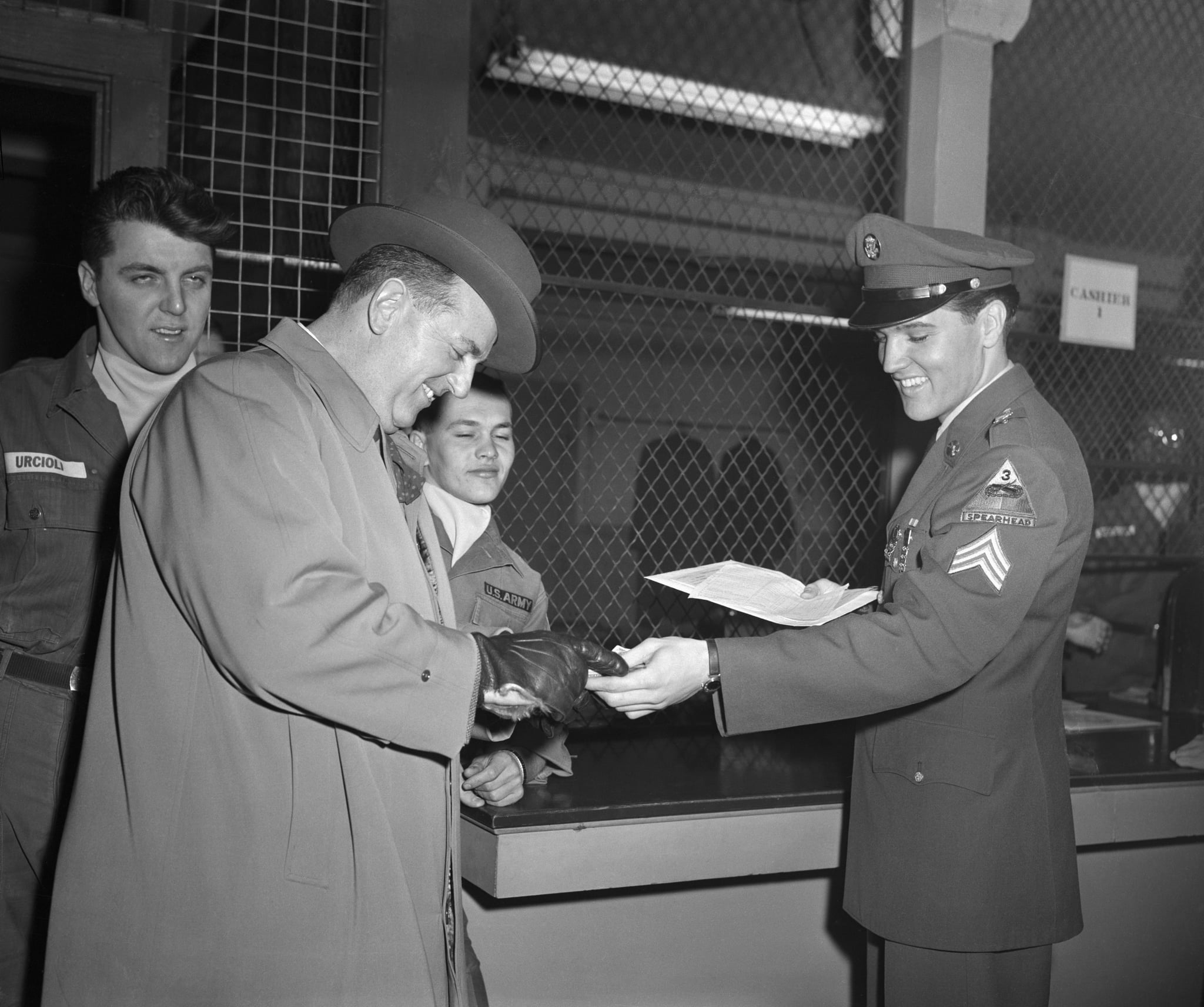 (Original Caption) 3/5/1960-Fort Dix, NJ- After being discharged from the US Army today, Elvis Presley (R) grins as he hands his mustering out pay to his business manager Colonel Tom Parker.